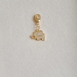 May include: Gold charm with a small elephant design, encrusted with clear rhinestones. The charm has a lobster clasp.