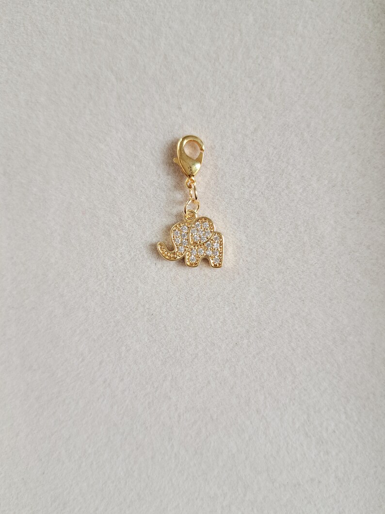 May include: Gold charm with a small elephant design, encrusted with clear rhinestones. The charm has a lobster clasp.