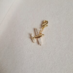 May include: Gold airplane charm with clear crystal accents. The charm has a lobster clasp for attaching to a bracelet or necklace.