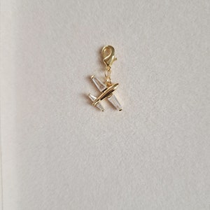 May include: Gold airplane charm with clear crystal accents. The charm has a lobster clasp for attaching to a bracelet or necklace.
