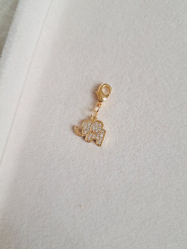 May include: A gold-tone elephant charm with clear rhinestones. The charm has a lobster clasp.