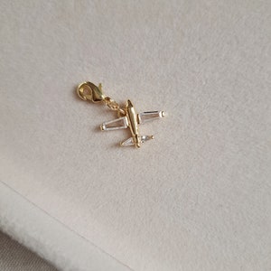 May include: Gold airplane charm with clear crystal accents. The charm has a loop for attaching to a bracelet or necklace.