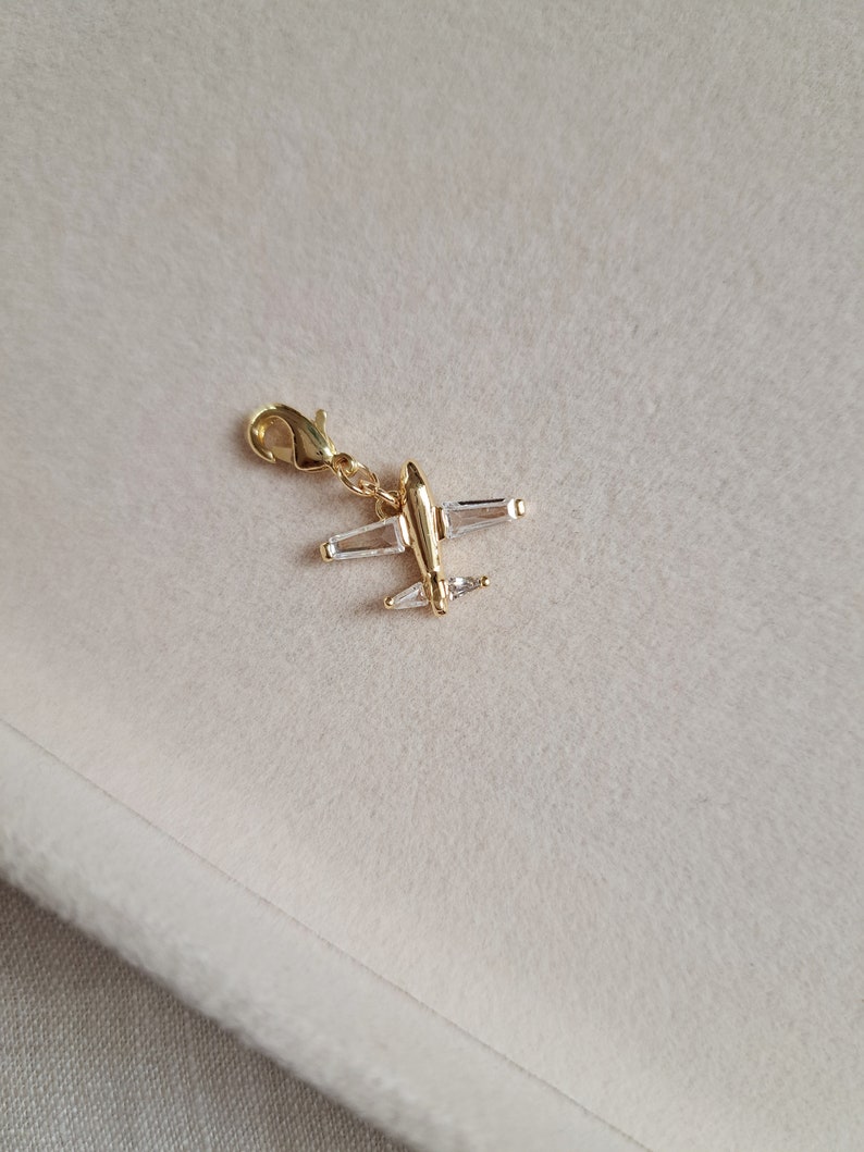May include: Gold airplane charm with clear crystal accents. The charm has a loop for attaching to a bracelet or necklace.