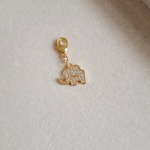 May include: Gold-tone elephant charm with clear crystal embellishments. The charm has a lobster clasp for attaching to a bracelet or necklace.