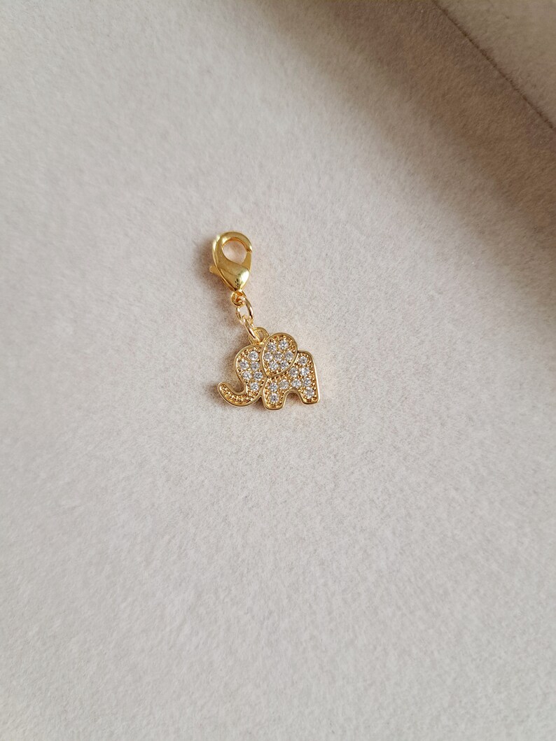 May include: Gold-tone elephant charm with clear crystal embellishments. The charm has a lobster clasp for attaching to a bracelet or necklace.