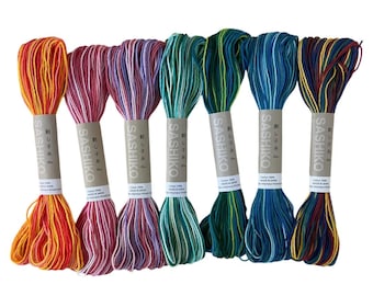 Op de afbeelding: Zeven strengen Sashiko-garen in verschillende kleuren, waaronder oranje, roze, groen en blauw. Elke streng is verpakt met een papieren etiket met Japanse tekst. De draden zijn gemaakt van katoen.