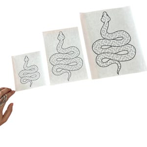 May include: Three white sheets of paper with a black line drawing of a snake with a checkered pattern on each sheet. The sheets are different sizes.