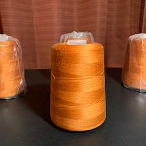 Op de afbeelding: Vier spoelen oranje draad, drie zijn verpakt in doorzichtig plastic en één is uitgepakt.