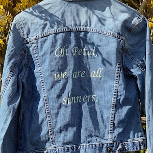 May include: A blue denim jacket with white embroidery on the back that reads "Oh Petal, we are all sinners."