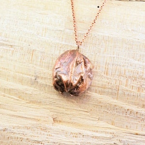 Könnte beinhalten: Eine Kupferkette mit einem Anhänger in Form einer Walnuss. Der Anhänger hat eine strukturierte, organische Optik.