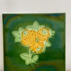 Peut inclure: Un carreau de céramique carré avec un fond vert et un motif floral jaune. Le carreau présente trois roses jaunes avec des feuilles vertes.