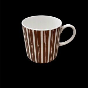 Puede incluir: Una taza de cerámica blanca con un patrón de rayas marrones y blancas. La taza tiene un asa redondeada.