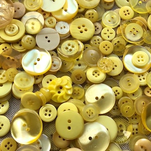 May include: A large collection of yellow buttons in various sizes and styles. The buttons are made from different materials, including plastic, metal, and wood.