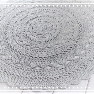 Peut inclure: Un tapis rond en crochet gris avec un motif circulaire. Le tapis a un design délicat et ajouré.