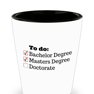 May include: White shot glass with a black rim. The text "To do:" is printed above a checklist with "Bachelor Degree" and "Masters Degree" checked off, and "Doctorate" unchecked.