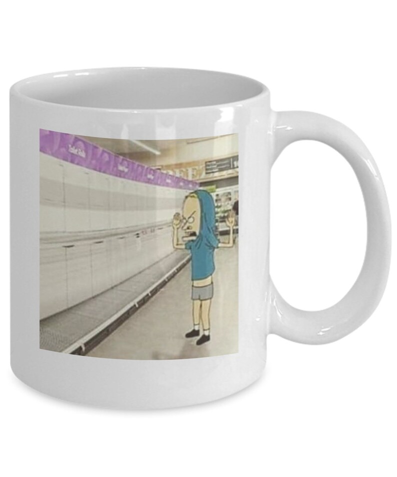 May include: White ceramic coffee mug with a cartoon image of a person in a blue hoodie standing in an empty grocery store aisle. The person is looking at the camera with a frustrated expression and has their hands raised in the air. The text "Toilet Paper" is visible on a shelf in the background.