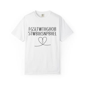 Puede incluir: Camiseta blanca con cuello redondo, texto negro y un diseño en forma de corazón con una cruz. La camiseta está hecha de un material suave. Una parte superior informal para el uso diario.