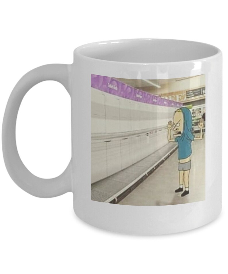 May include: A white ceramic coffee mug with a cartoon image of a person in a blue shirt and shorts standing in an empty grocery store aisle. The text "Toilet Paper" is visible on a shelf in the background.
