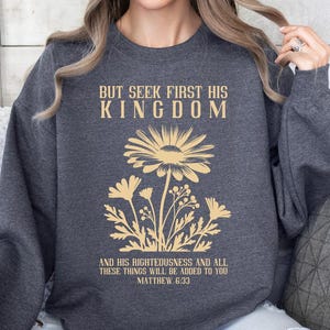 May include: A dark gray sweatshirt with a floral design and the text "But seek first his kingdom and his righteousness and all these things will be added to you Matthew 6:33".