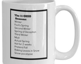 May include: White ceramic coffee mug with a black border and text that reads "The 11 OHIO Seasons: Winter, Fool's Spring, Second Winter, Spring of Deception, Third Winter, Mud, Actual Spring, Hot for 2 weeks, Pretend Fall, Raking Leaves in Snow, Snow-pocalypse".
