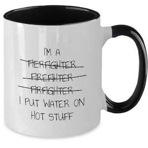 May include: White coffee mug with a black rim and handle. The mug has black text that reads "I'm a Firefighter I put water on hot stuff" with the word "Firefighter" crossed out three times.