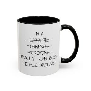May include: White ceramic mug with a black rim and handle. The mug has black text that reads "I'm a". The words "Corporal", "Corpral", and "Coreport" are crossed out. The text continues with "Finally I can boss people around".