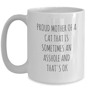 May include: White ceramic mug with a curved handle. The mug features black text that reads: "PROUD MOTHER OF A CAT THAT IS SOMETIMES AN ASSHOLE AND THAT'S OK."