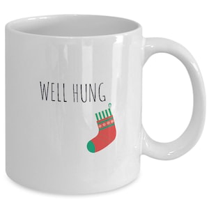 May include: White ceramic coffee mug with the text "WELL HUNG" and a red and green Christmas stocking hanging from the text.