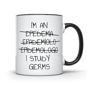 Pu&ograve; includere: Tazza in ceramica bianca con manico e bordo neri. La tazza presenta la scritta "I'M AN... I STUDY GERMS" in nero, con parole cancellate sopra "I STUDY GERMS".