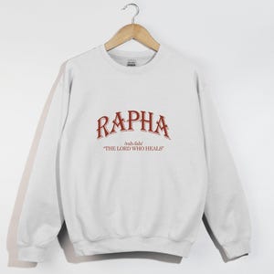 May include: White sweatshirt with a red graphic print that says "RAPHA" with the pronunciation "rah-fah" and "THE LORD WHO HEALS" underneath.
