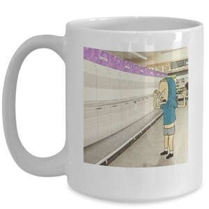 May include: White ceramic coffee mug with a cartoon image of a person in a blue shirt and grey shorts standing in an empty grocery store aisle. The text "Toilet Paper" is visible on a purple sign above the aisle.