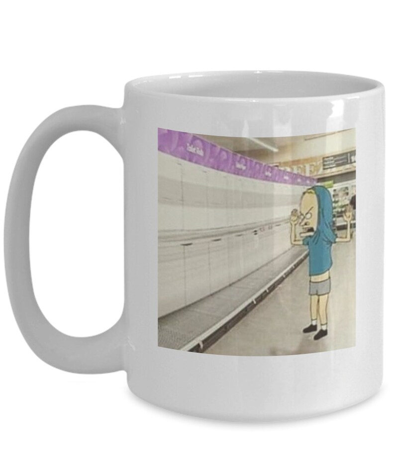 May include: White ceramic coffee mug with a cartoon image of a person in a blue shirt and grey shorts standing in an empty grocery store aisle. The text "Toilet Paper" is visible on a purple sign above the aisle.