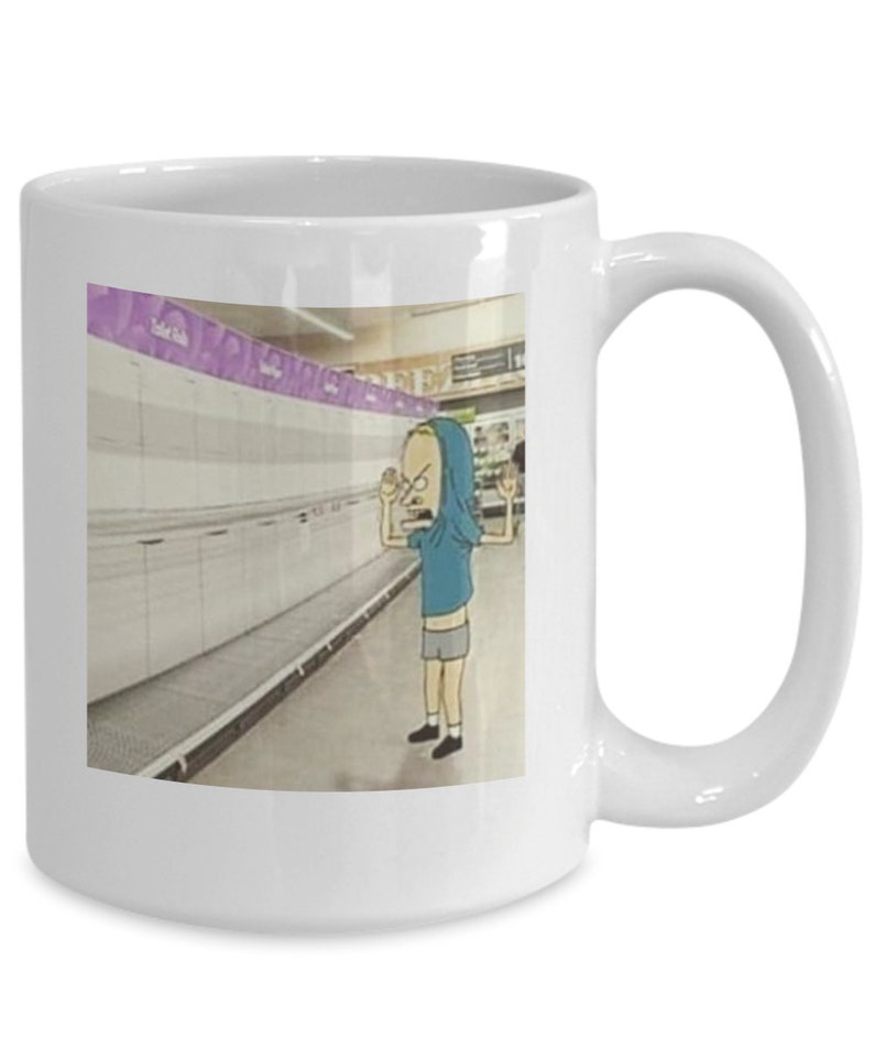 May include: White ceramic coffee mug with a cartoon image of a person in a blue hoodie standing in a grocery store aisle with empty shelves. The person is looking at the camera with a frustrated expression.