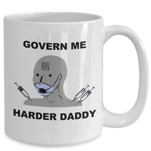 May include: White ceramic mug with the text "GOVERN ME HARDER DADDY" in black. The mug features a gray cartoon figure wearing a blue face mask and holding syringes. A QR code is above the figure's head.