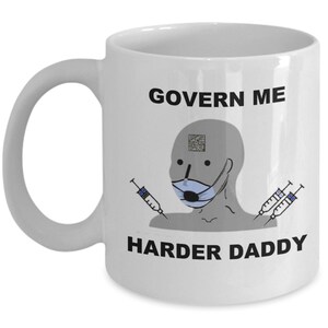 May include: White ceramic mug with a handle. The mug features a meme-style graphic with a masked face, syringes, and the text "GOVERN ME HARDER DADDY" in black. The mug is designed for hot or cold drinks.