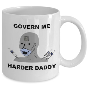 May include: White ceramic mug with a humorous design. The mug features the text "GOVERN ME HARDER DADDY" with a cartoon figure wearing a face mask and syringes. The mug has a curved handle.