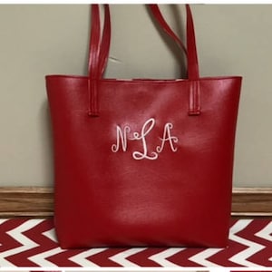 Könnte beinhalten: Rote Einkaufstasche mit weißen Ledergriffen und einem weißen gestickten Monogramm "N.L.A."