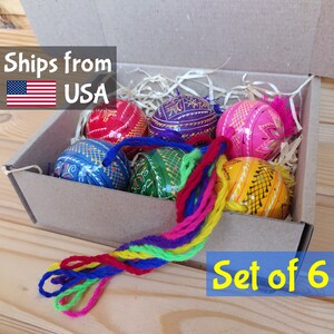 May include: Set of six hand-painted wooden Easter eggs in a brown cardboard box with shredded paper. The eggs are decorated with colorful geometric patterns and have a tassel of multi-colored yarn.