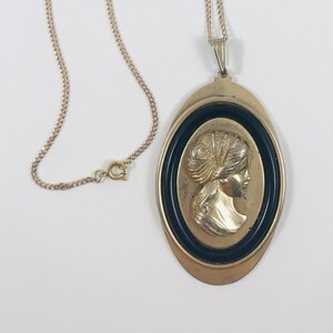 May include: A gold chain necklace with a pendant featuring a black cameo of a woman's profile.