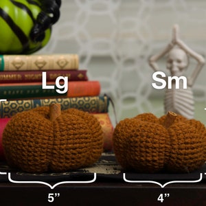 May include: Two crocheted pumpkins, one labeled "Lg" and measuring 5 inches wide and 3 inches tall, and the other labeled "Sm" and measuring 4 inches wide and 2.5 inches tall.