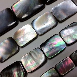 May include: Rectangular mother-of-pearl beads with iridescent colors. The beads have a polished, glossy finish, reflecting light with hues of black, silver, green, and pink. These beads are ideal for jewelry making.