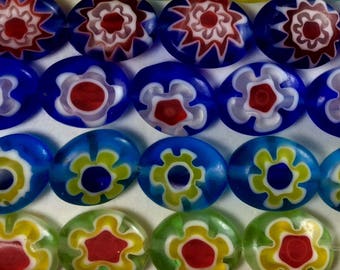 May include: Oval-shaped glass beads with colorful floral patterns. The beads are blue, green, and white with red, yellow, and blue accents.