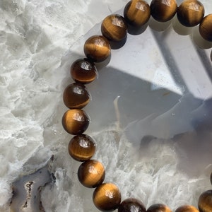 May include: A brown and gold tiger's eye beaded bracelet. The beads are round and have a glossy finish.