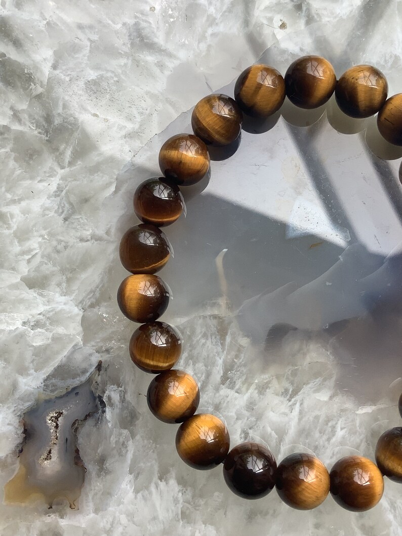 May include: A brown and gold tiger's eye beaded bracelet. The beads are round and have a glossy finish.