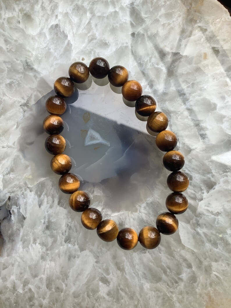 May include: A brown and gold tiger's eye beaded bracelet. The bracelet is made of round beads and is strung on a clear elastic cord.