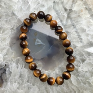 May include: A brown and gold tiger's eye beaded bracelet on a white background.