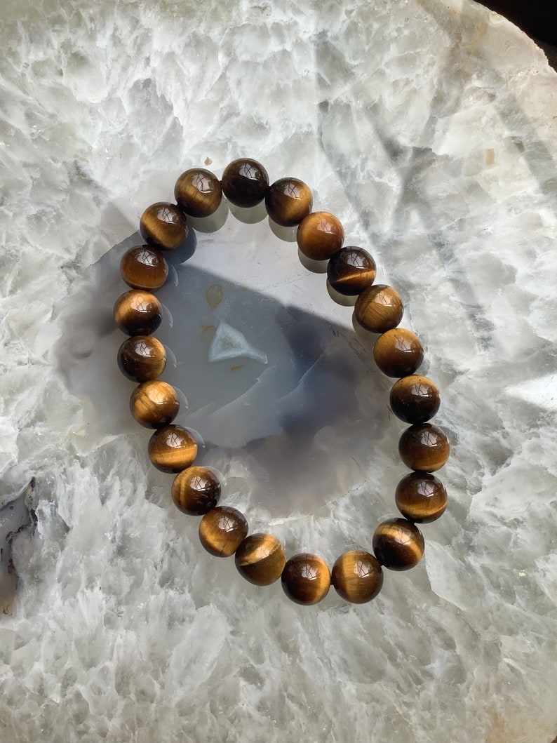 May include: A brown and gold tiger's eye beaded bracelet on a white background.