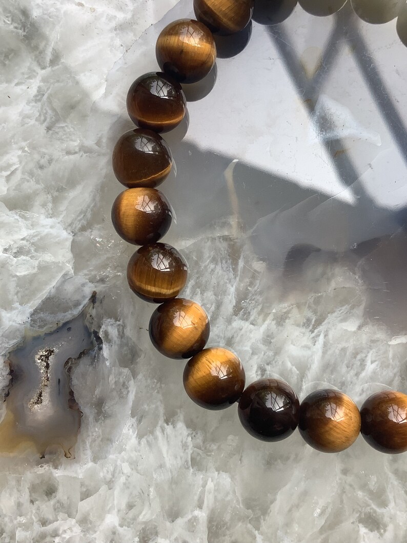 May include: A brown and gold tiger's eye beaded bracelet. The beads are round and smooth, and the bracelet is strung on a clear elastic cord.