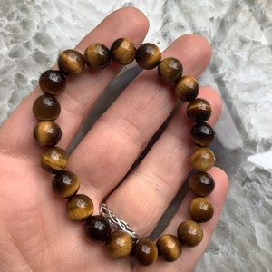 May include: A brown and gold tiger's eye beaded bracelet. The bracelet is made of round beads and is strung on elastic.