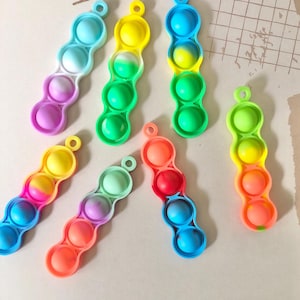May include: Seven colourful silicone fidget toys with a three-bubble design. Each toy has a different colour gradient and is shaped like a long, thin bean.